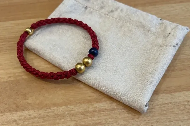 Pulsera sencilla de cordón rojo junto a una bolsa de lino