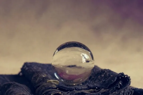 Esfera de cristal transparente reposa sobre tela oscura en luz indirecta