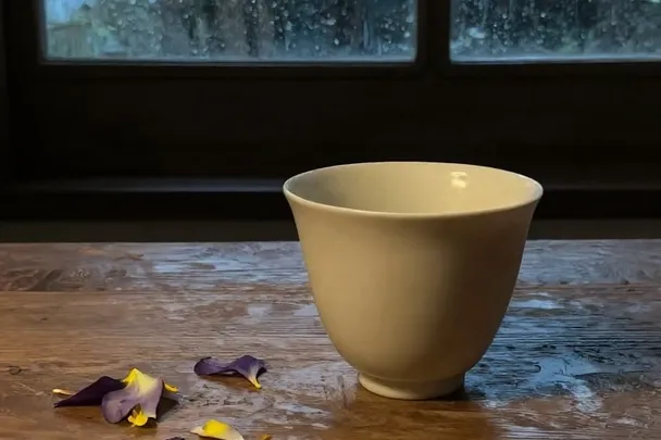 Taza vacía y pétalos caídos sobre una mesa junto a la lluvia.