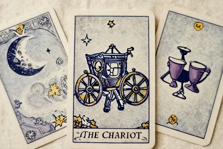 Tres cartas ilustradas con El Carro en el centro, una luna y dos copas