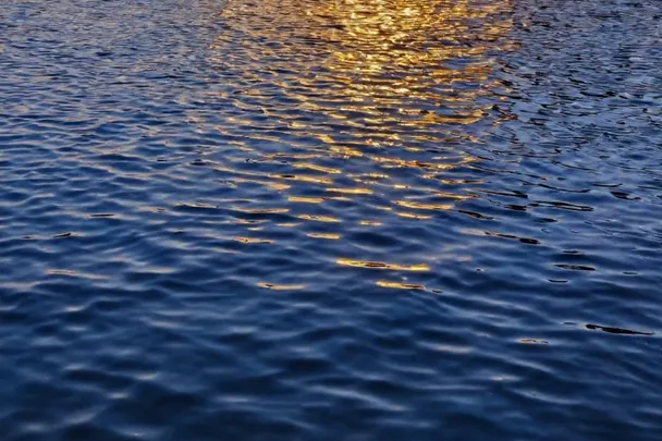 Luz ámbar se refleja en agua azul junto a una piedra volcánica
