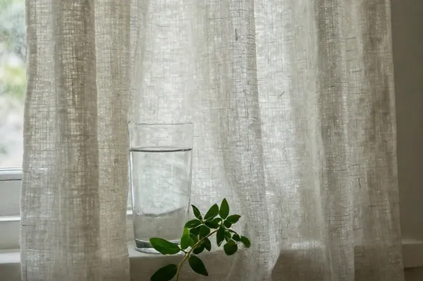 Cortina de lino junto a un vaso de agua en una ventana abierta.