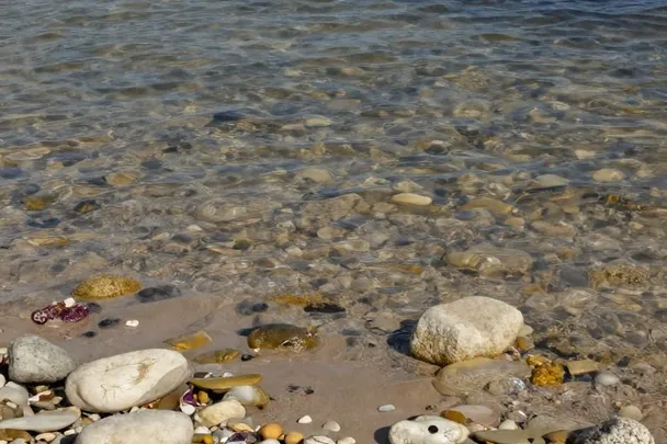Arena húmeda y piedras ordenadas junto a agua ondulada.