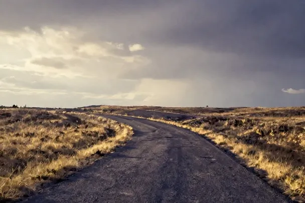 Camino curvo entre campos bajo un cielo que empieza a despejar.