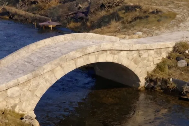 Puente de piedra sólido que cruza un arroyo hacia campos abiertos.