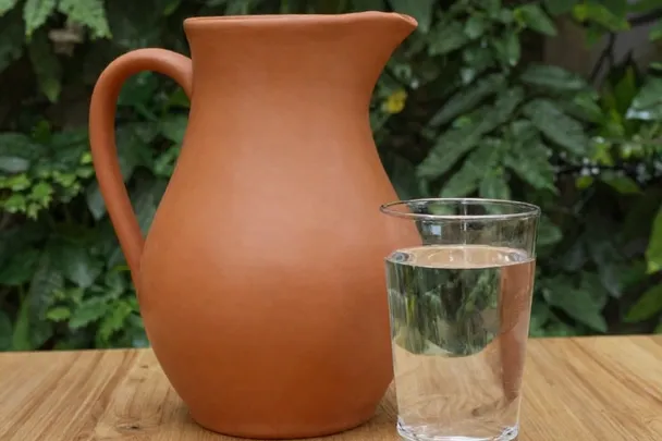 Jarra de barro y vaso sencillo sobre una mesa maciza.