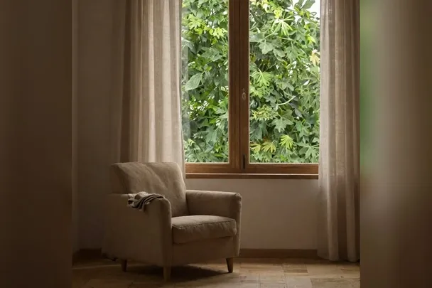 Sillón vacío junto a una ventana con cortinas de lino.
