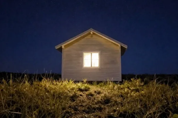 Luz cálida en la ventana de una cabaña bajo el cielo nocturno.