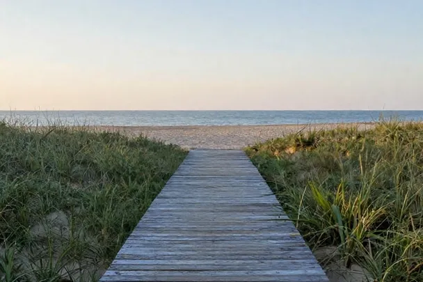 Pasarela de madera que comienza junto a una playa tranquila.