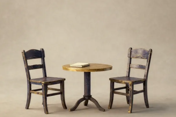 Two empty chairs face each other across a small table with a closed notebook.