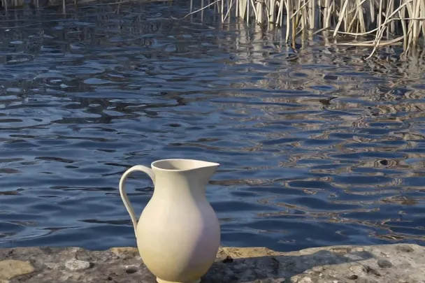 A plain water pitcher rests beside a rippling pool in clear winter light.