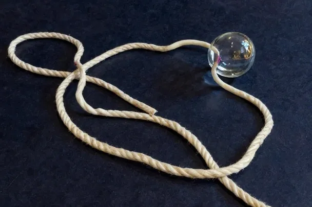 A long loose cord curves across a dark reading table beside a clear lens.