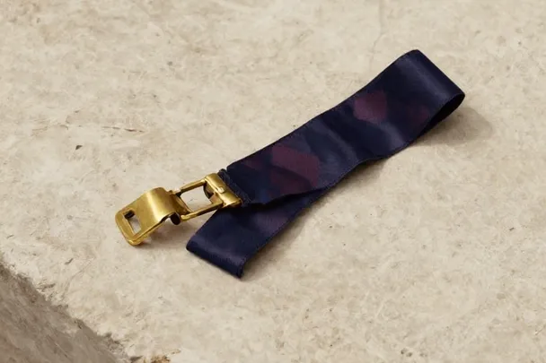 An open brass clasp lies beside a loose ribbon on pale stone.