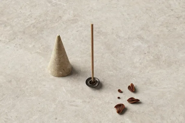 Una varilla de incienso apagada, un cono y pequeños fragmentos aromáticos secos sobre piedra clara.
