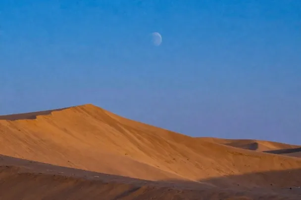 Cielo de amanecer con la luna desvaneciéndose sobre las dunas.