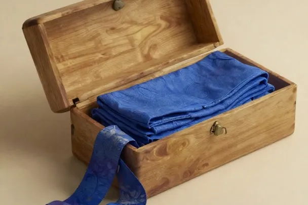 Cinta suelta sale de una caja de madera entreabierta junto a una tela azul