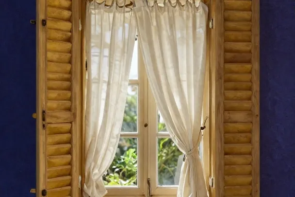 Cortina retirada deja ver una ventana restaurada abierta a un jardín