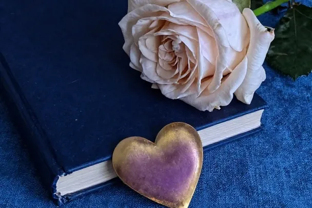 Rosa abierta reposa sobre una tela azul junto a un libro cerrado