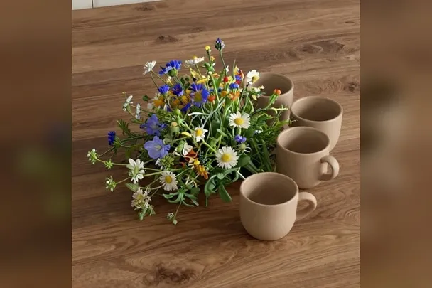 Ramo de flores silvestres junto a tazas de barro en una mesa.