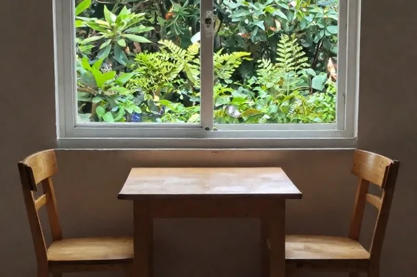 Sillas vacías separadas por una mesa pequeña junto a una ventana.