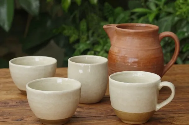 Tazas distintas con una misma jarra sobre una mesa sencilla.