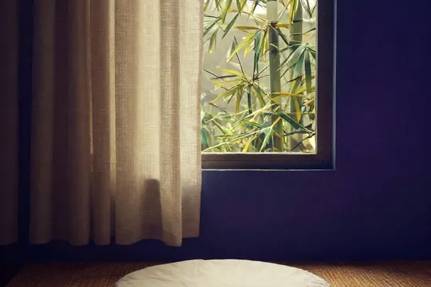 Cojín de meditación sobre una esterilla junto a una ventana.