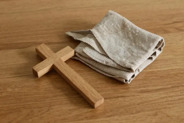 Cruz de madera junto a lino doblado sobre una mesa.