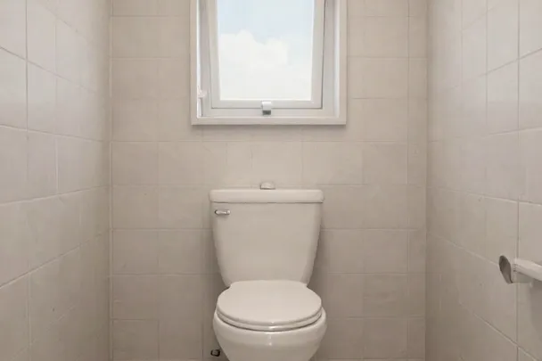 Inodoro cerrado en un baño limpio con una ventana alta.