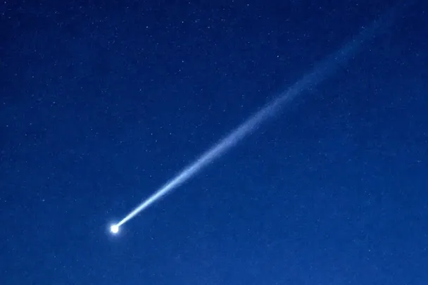 Estrella fugaz con una estela recta sobre un horizonte nocturno.