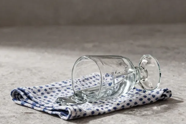 Vaso volcado derrama agua junto a un paño sobre baldosas