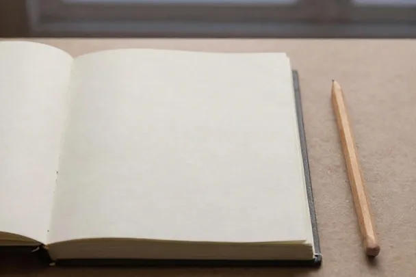 Cuaderno abierto y lápiz junto a una ventana.