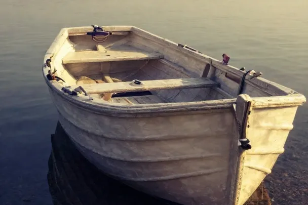 Barca de madera vacía reposa junto a una orilla de aguas tranquilas