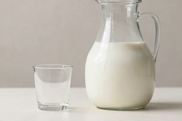 Jarra de vidrio con leche junto a un vaso.