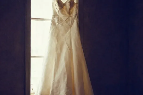 Vestido blanco sencillo cuelga junto a una ventana luminosa
