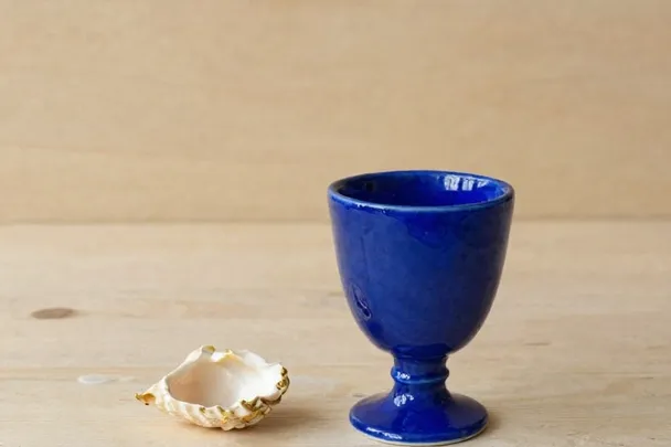Copa azul junto a una concha en una mesa de madera clara
